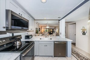 Une cuisine moderne dotée d’appareils électroménagers en acier inoxydable, d’un grand îlot central avec un évier et donnant sur l’espace de vie.