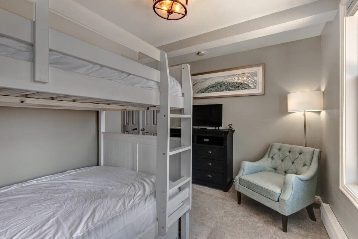 A bunk bed room with a ladder, a dresser, a chair, and a painting on the wall.