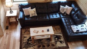 Ein gemütliches Blockhausschlafzimmer mit einer schwarzen Ledersofa, einem Holztisch und einem Tierfellteppich.