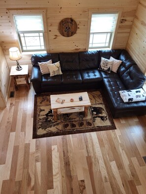 A cozy cabin interior with a black leather sofa, a wooden coffee table, and a rug with animal prints.