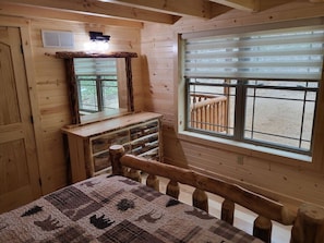 A wooden cabin room with a bed, a dresser, a mirror, and a window with a view of a wooden deck. - Jack of Hearts. Secluded, Hocking Hills cabin! (Rockbridge)