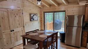 Ein Holzblockbau-Innenraum mit Esstisch, Stühlen, einem Kühlschrank und einem großen Fenster mit Blick auf eine Terrasse.