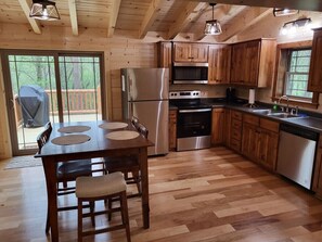 Cocina de cabaña de madera con una isla grande, electrodomésticos de acero inoxidable y una puerta corrediza de vidrio al exterior.