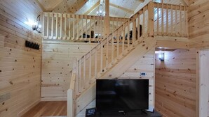 Ein Holzblockhaus-Interieur mit Fernseher, Holzböden, einer Treppe und einem Balkon.