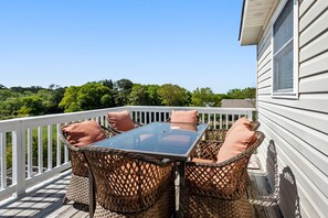 Une terrasse dotée de meubles en osier et d’une table en verre, offrant une vue sur une zone boisée.