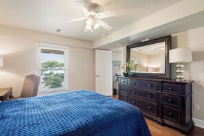 Une chambre à coucher avec un lit, une commode, un miroir et un ventilateur de plafond.
