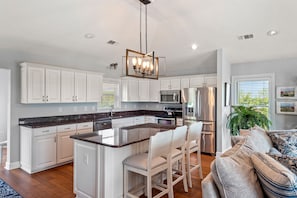 A modern kitchen with white cabinets, a granite countertop, and stainless steel appliances. There is a bar area with stools and a large island.