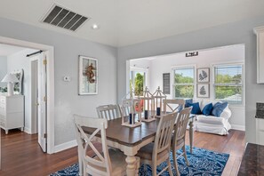 A dining area with a wooden table and chairs, a white sofa, and a blue patterned rug. - Worthington Lane: Pool, Hot Tub, Golf Course View (Kitty Hawk)