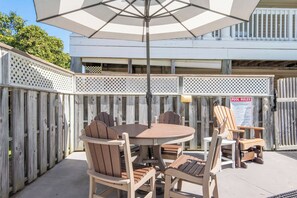 Une terrasse extérieure avec une table ronde et des chaises, un grand parasol et un panneau indiquant les règles à respecter à la piscine.