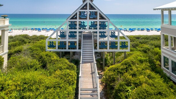 Une maison de plage avec un escalier menant à une terrasse agrémentée de parasols bleus.