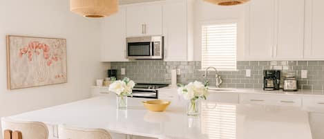 Una cocina moderna con armarios blancos, una isla central con sillas, un microondas y una cafetera.
