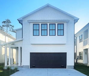 A two-story house with a garage, a covered porch, and a brick facade. - Coastal Home · Bay Views · Near the Wharf · Pet Friendly (Orange Beach)
