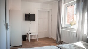 A bedroom with a bed, a TV mounted on the wall, a window with curtains, and a radiator. - House Morgentau centrally located with garden (Kassel)