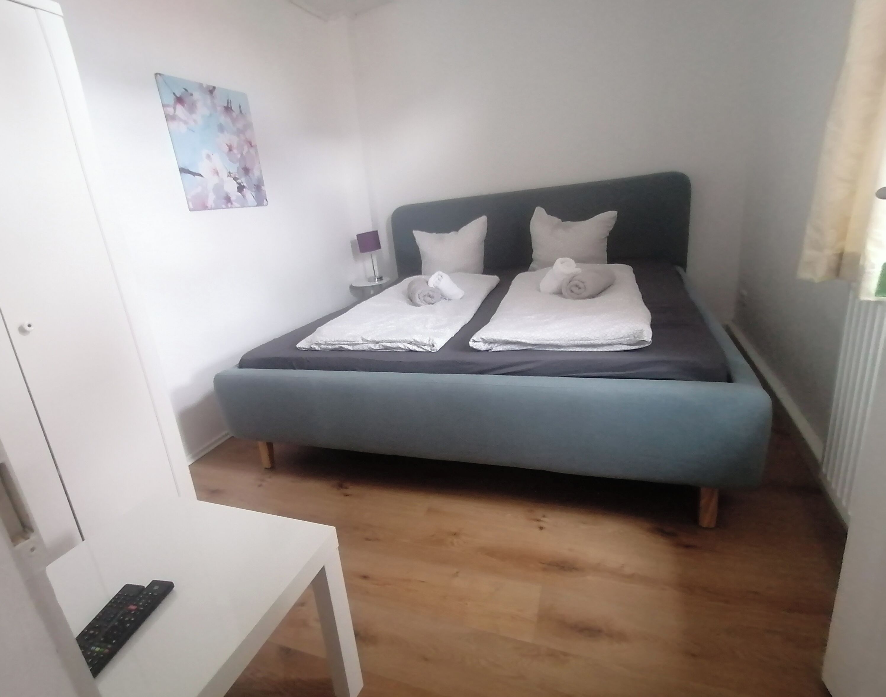 A bedroom with a bed, pillows, a bedside table, a lamp, and a painting on the wall.