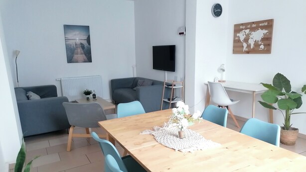 A modern living room with a wooden dining table, blue chairs, a grey sofa, a flat-screen TV, and a world map on the wall. - House Morgentau centrally located with garden (Kassel)