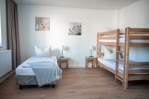 A bedroom with a single bed, a bunk bed, two bedside tables, and two wall-mounted lamps.