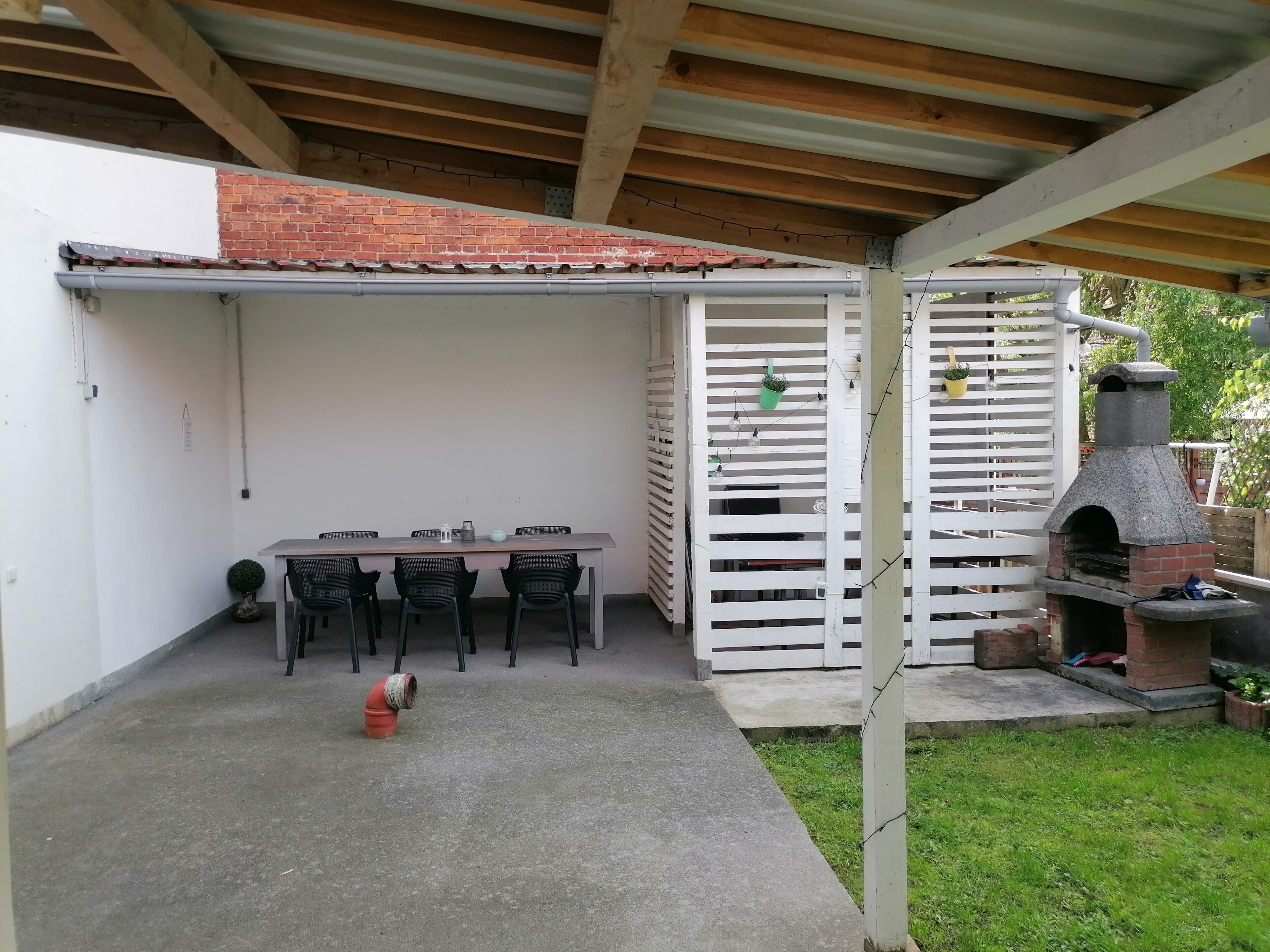 Un patio cubierto con una mesa y sillas, un horno de ladrillo y una valla blanca.