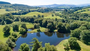 An aerial view of a lush green landscape with a lake surrounded by dense trees and rolling hills. - Mill House - self catering sleeps 10 (Crieff)
