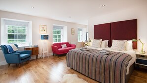 A bedroom with a large bed, a red chair, a blue armchair, and a wooden floor. - Mill House - self catering sleeps 10 (Crieff)