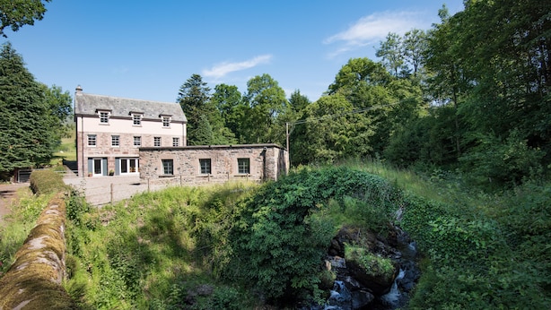 A stone house with a stone bridge over a stream, surrounded by lush greenery. - Mill House - self catering sleeps 10 (Crieff)