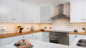 A modern kitchen with white cabinets, a stainless steel stove, and a wooden countertop. - Mill House - self catering sleeps 10 (Crieff)