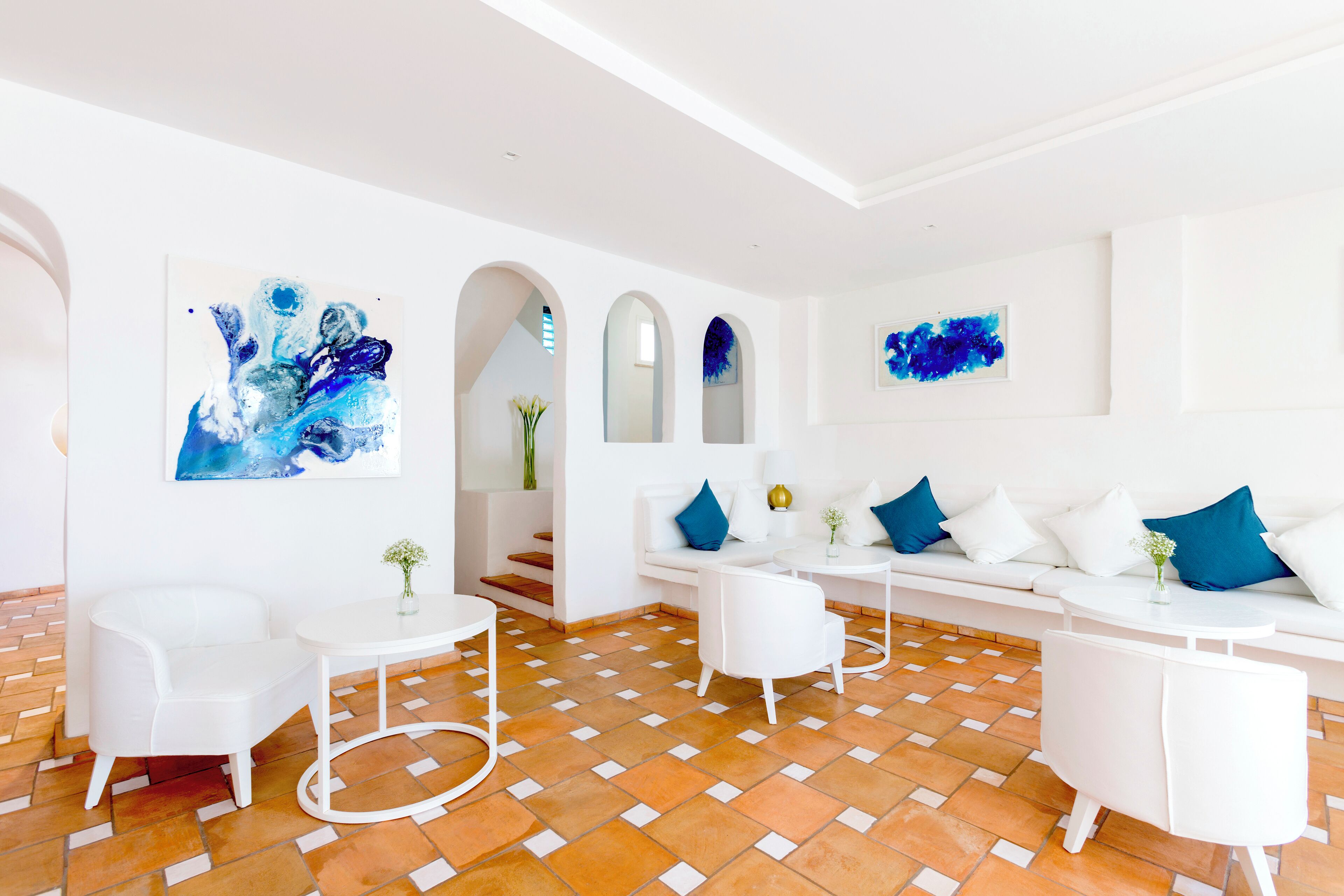 A modern living room with white furniture, a patterned floor, and abstract art on the walls.