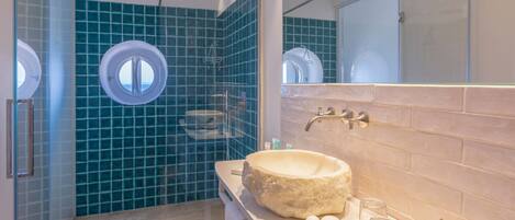 Une salle de bain avec un lavabo rond, une cabine de douche en verre et un grand miroir.