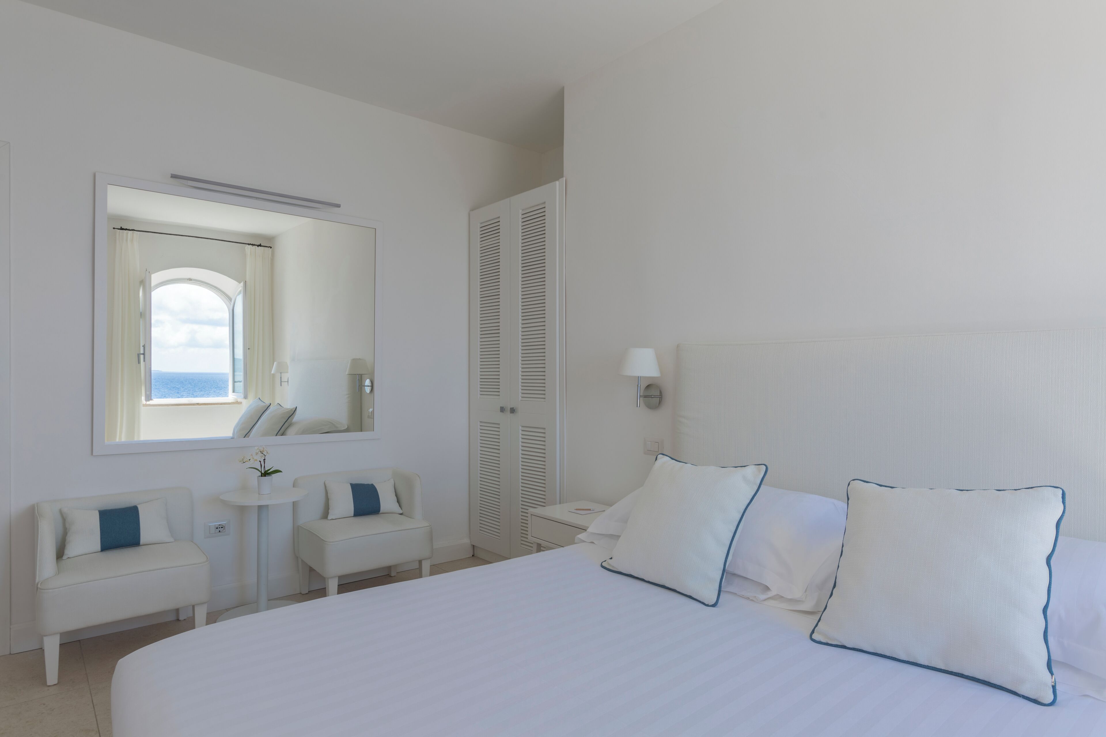 A hotel room with a large bed, two bedside tables, a sofa, a small table, and a wardrobe.