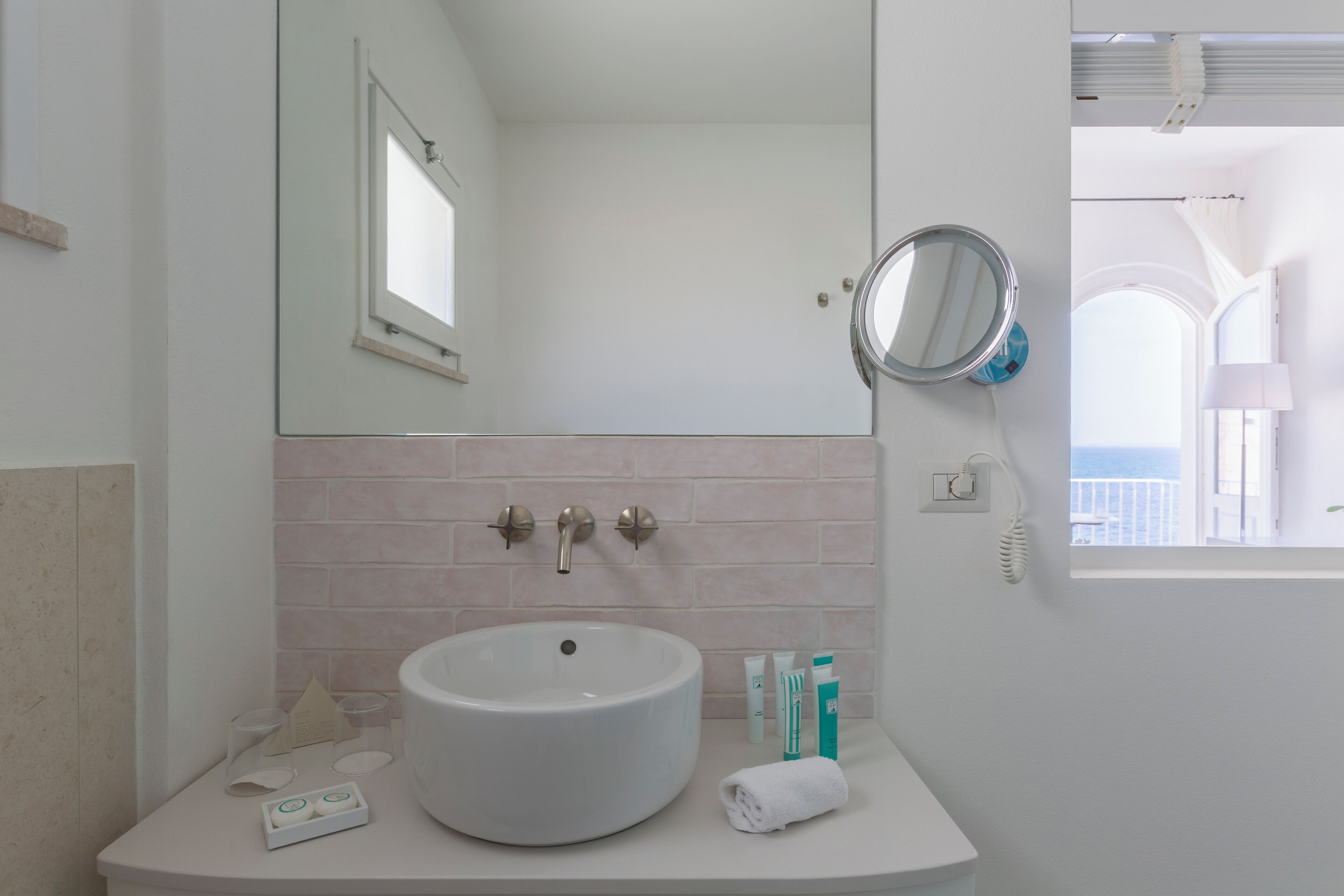 Un baño con un lavabo blanco grande, un espejo y una ventana con vista al mar.