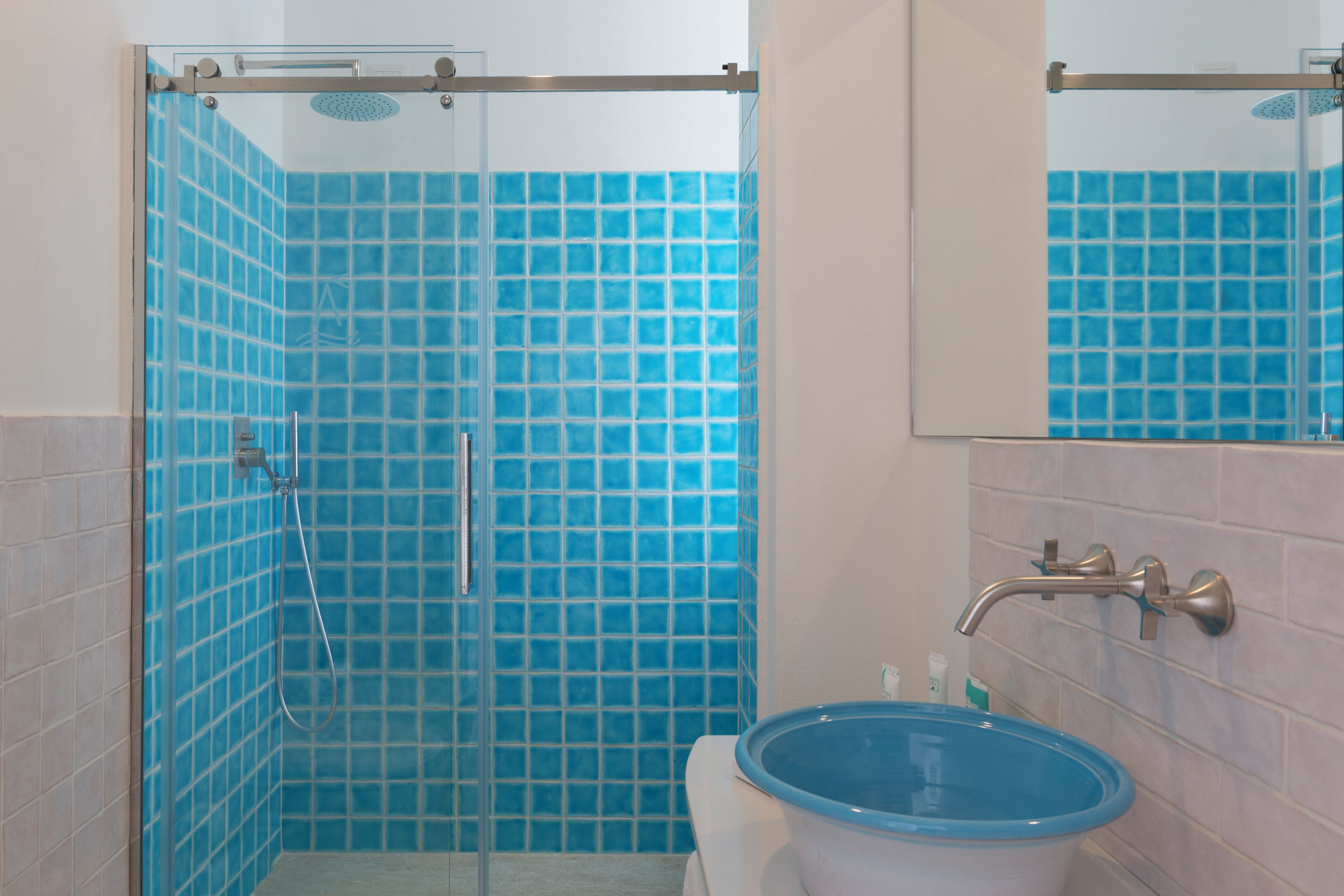 Un baño con paredes de azulejos azules, una cabina de ducha de vidrio y un lavabo con lavamanos azul.