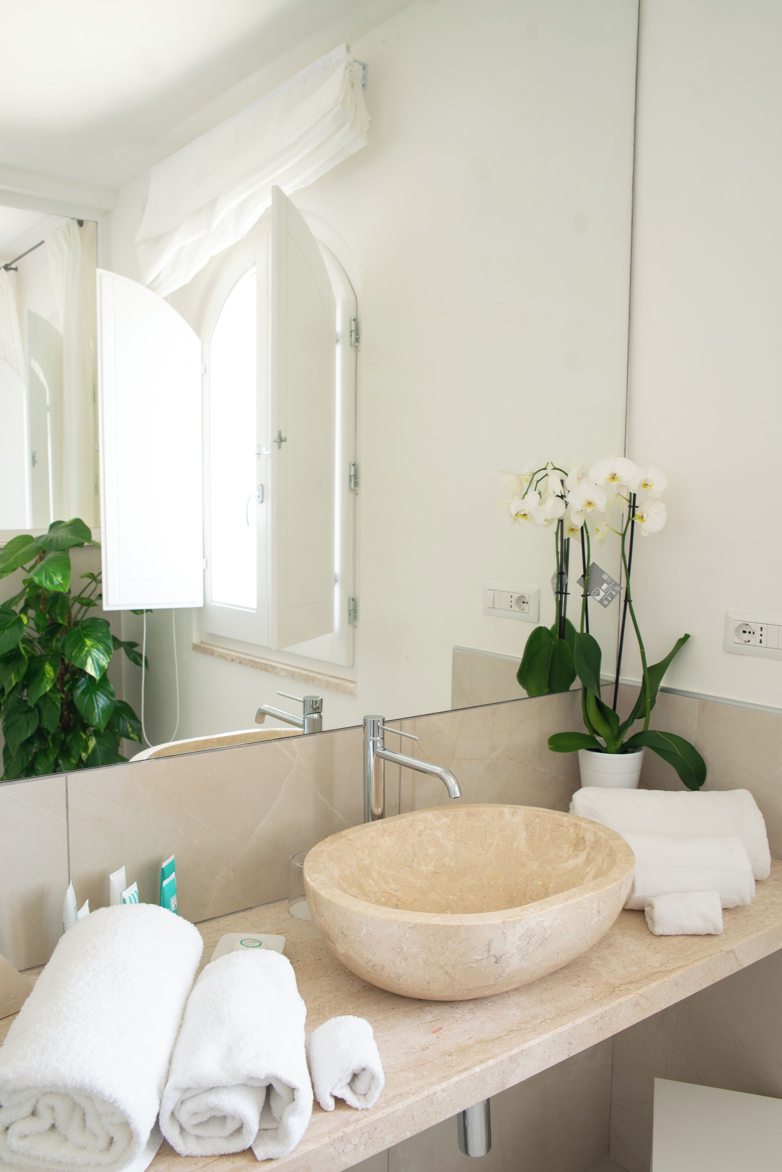 Une salle de bain avec un grand miroir, un lavabo beige et une orchidée en pot.
