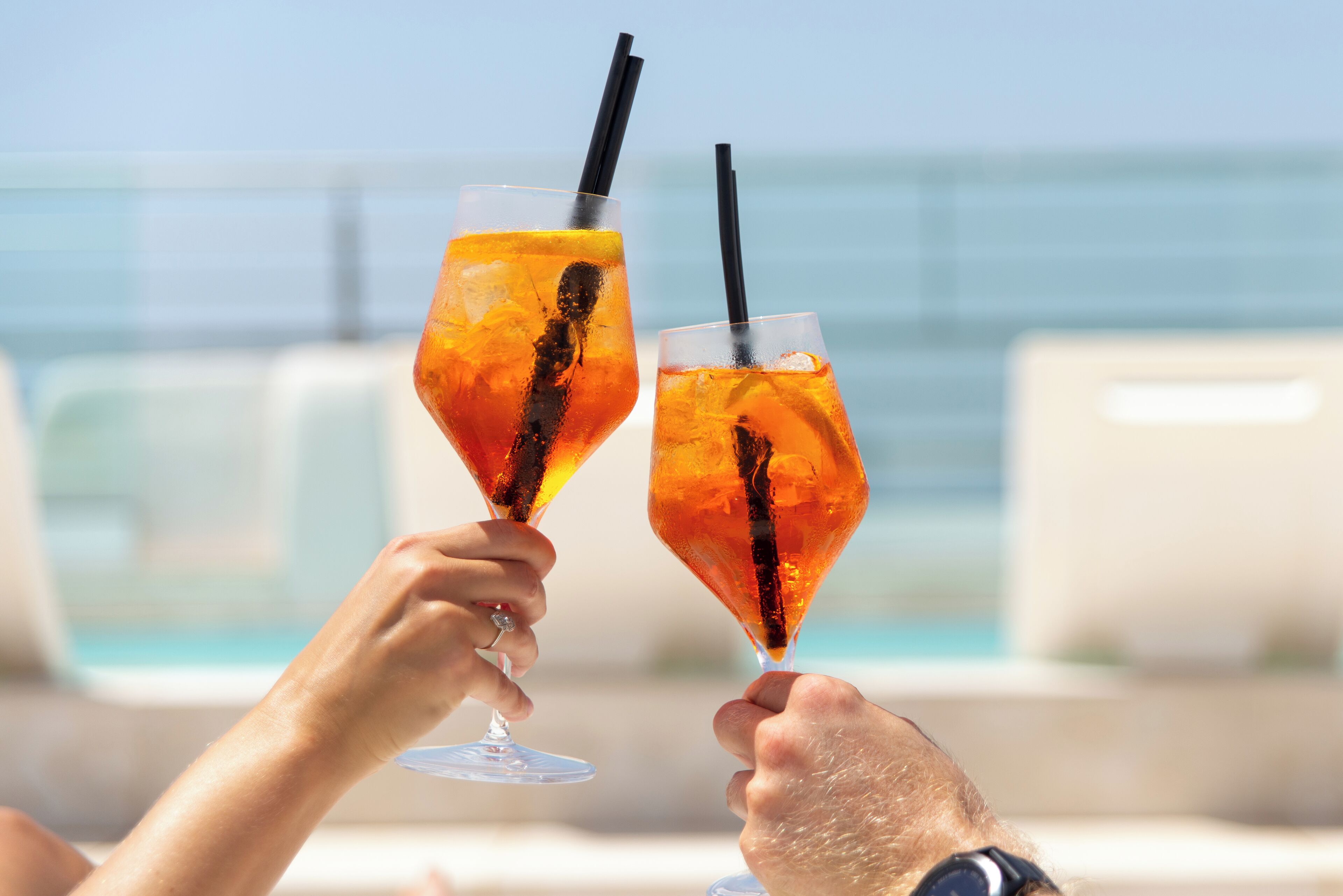 Dos personas brindando con bebidas junto a una piscina.