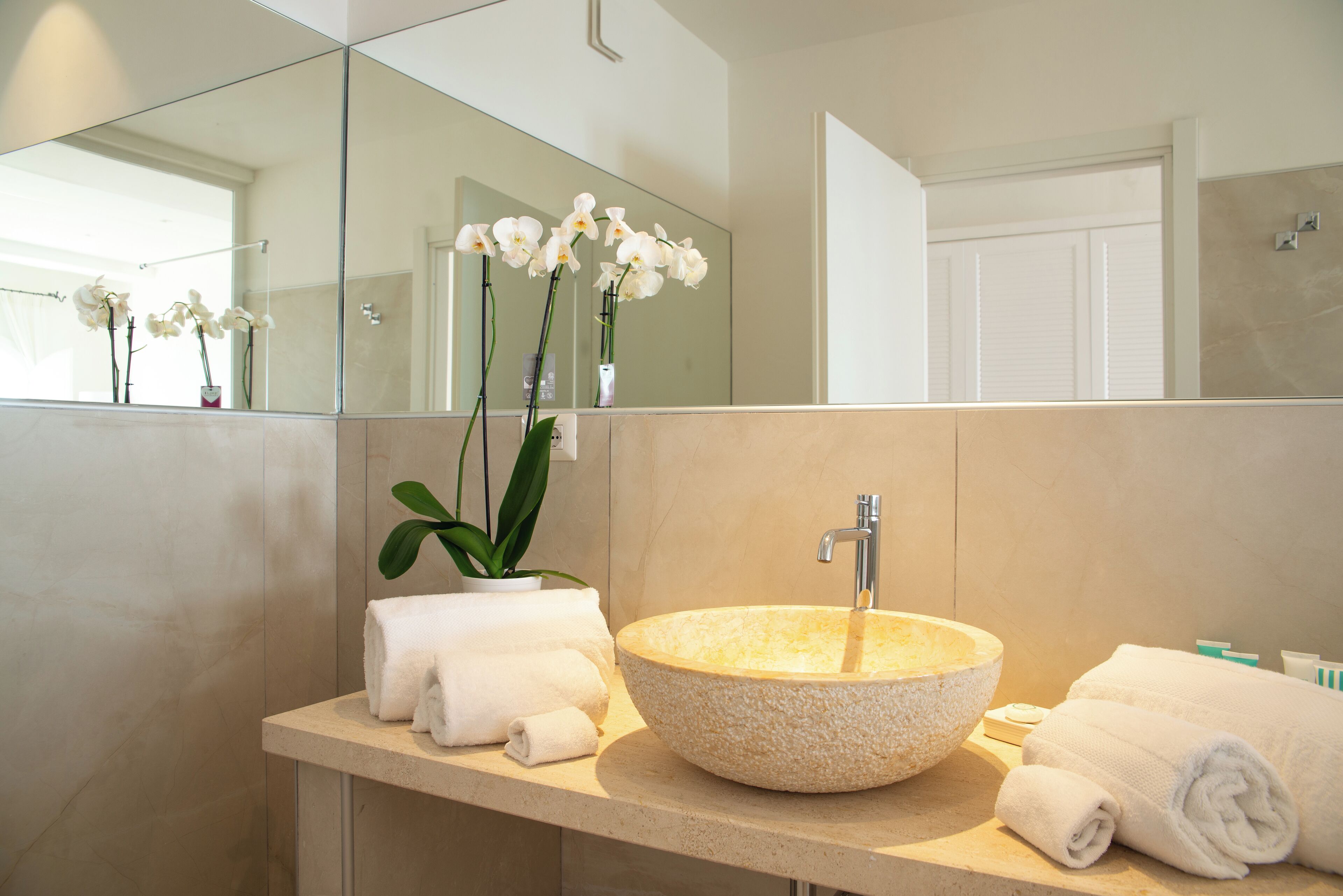 A bathroom with a round stone sink, white towels, and a potted orchid.