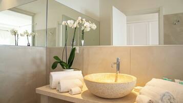 A bathroom with a round stone sink, white towels, and a potted orchid.