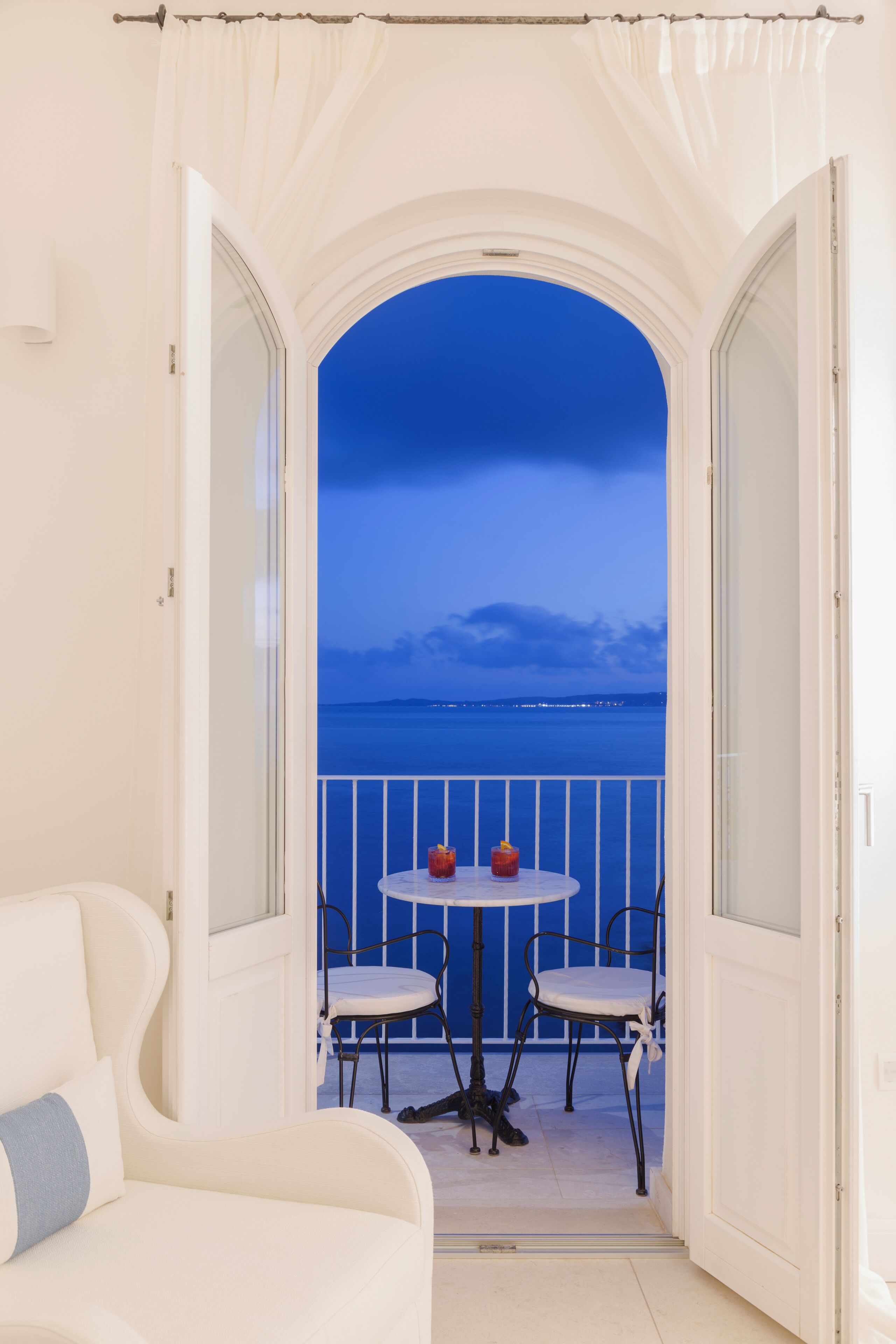Un balcon avec vue sur la mer, un canapé blanc et deux fauteuils.