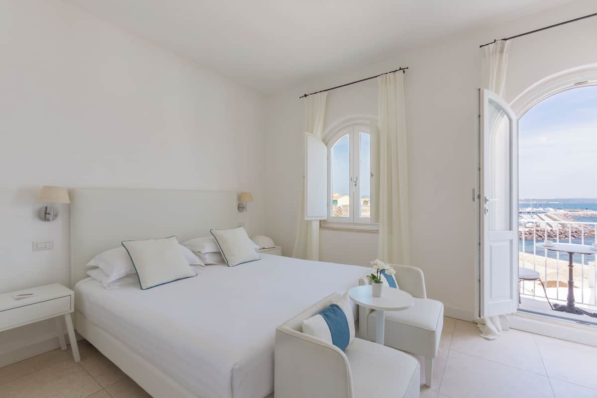 A hotel room with a large bed, a small table, and a balcony with a view.