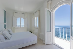 A bedroom with a large bed, two windows, and a balcony with a view of the sea. - Relais la Ghinghetta (Portoscuso)