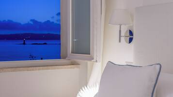 Ein Hotelzimmer mit Bett, Nachttisch, Lampe, Spiegel und Fenster mit Blick auf ein Gewässer im Abenddämmerung.