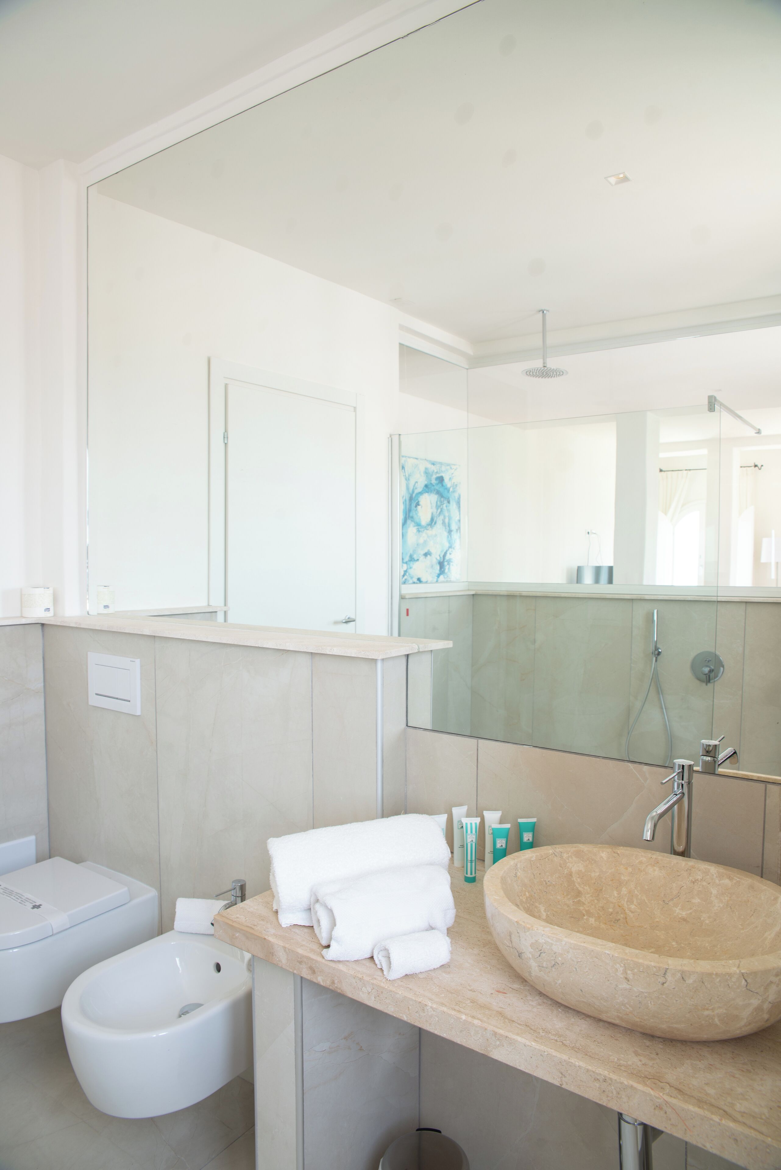 A modern bathroom with a large mirror, a beige sink, a bidet, and a toilet.
