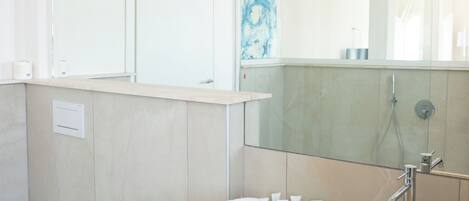 Un baño moderno con un espejo grande, un lavamanos color beige, un bidé y un inodoro.