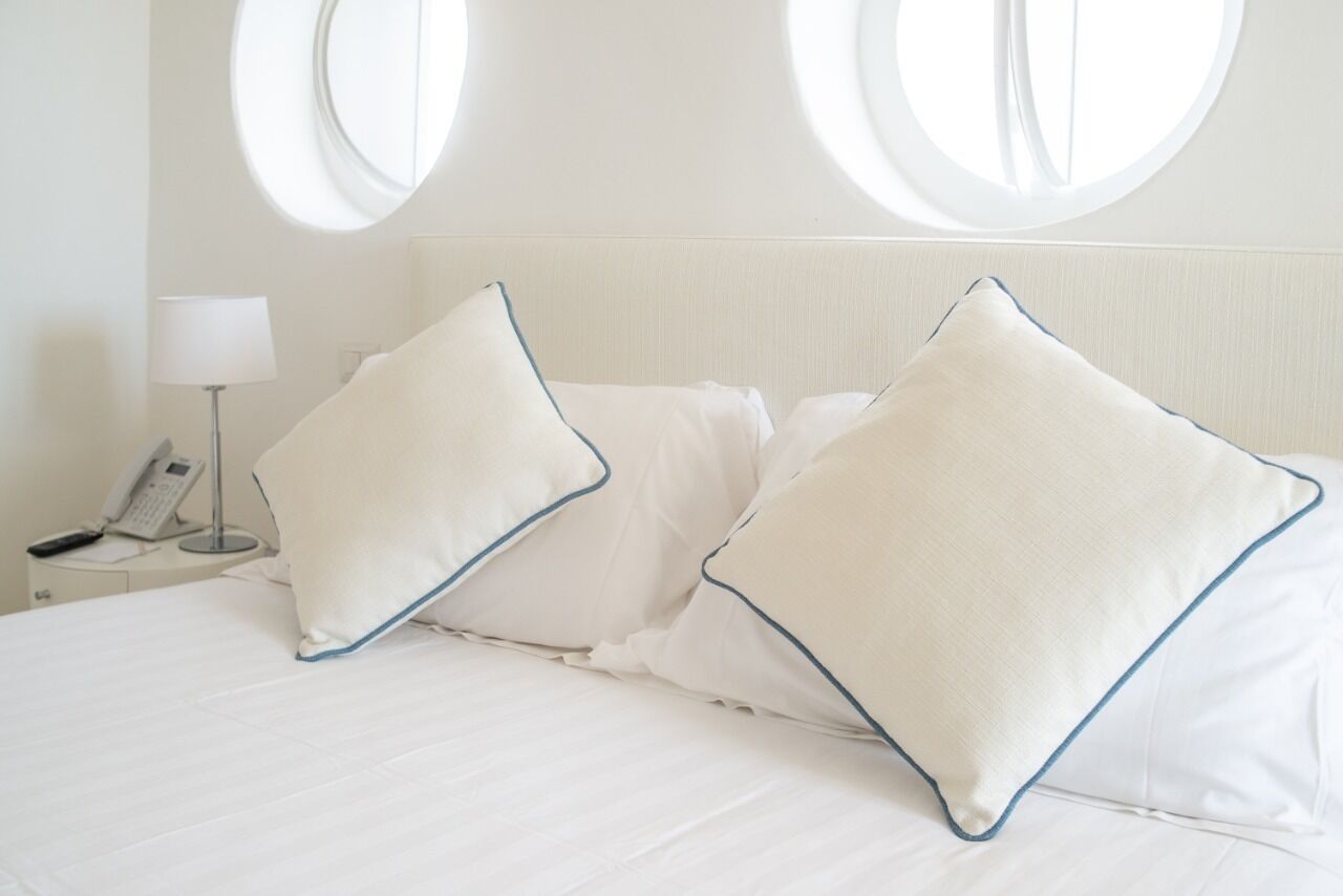 A hotel room with a bed, two pillows, a bedside lamp, and a phone on a nightstand.