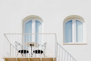 A balcony with a table and chairs, two arched windows, and a white railing. - Relais la Ghinghetta (Portoscuso)