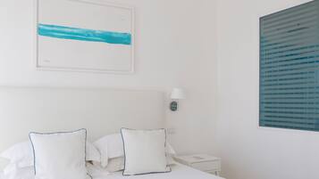 A neatly made bed with white linens and two pillows, a bedside table with a lamp, and a framed abstract painting on the wall.
