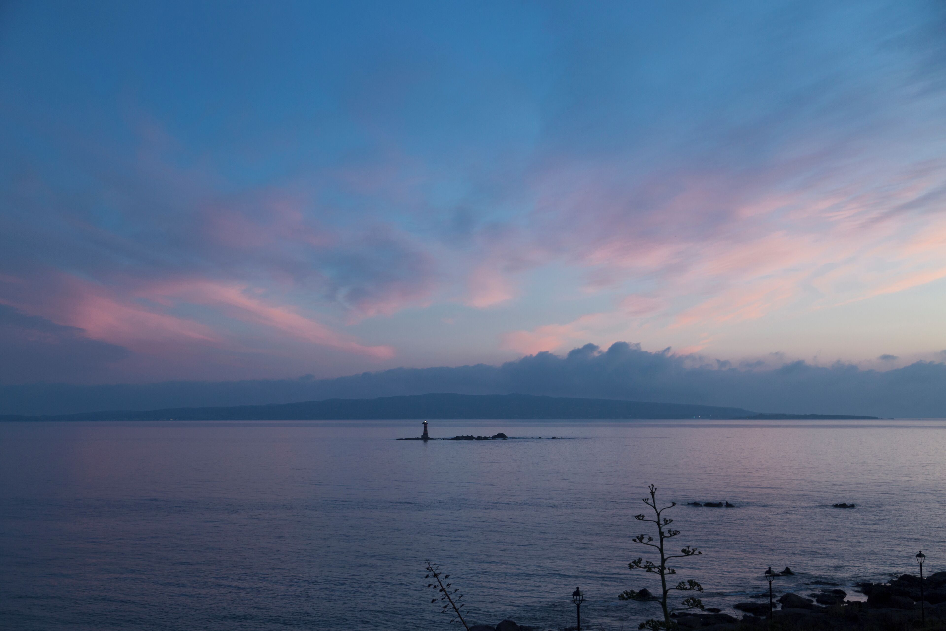 A calm body of water with a distant island and a lighthouse.
