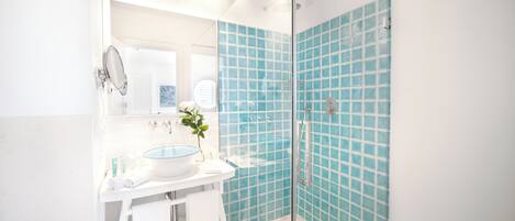 Un baño con ducha envuelta en vidrio, un lavabo blanco con recipiente azul y un espejo sobre el lavabo.