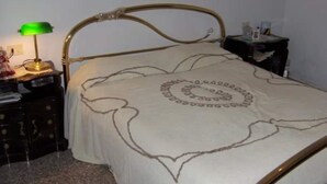 Una cama con un diseño circular en el colchón, una lámpara de escritorio verde y una pequeña mesa con una botella.