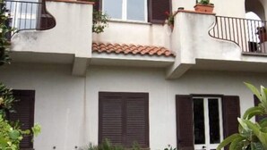 Un edificio de dos pisos con balcones, plantas en macetas y techo de tejas.