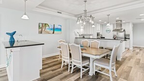 Eine moderne Küche mit weißen Schränken, einer zentralen Kochinsel und einem Essbereich mit Holztisch und gepolsterten Stühlen.