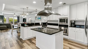 Eine moderne Küche mit weißen Schränken, einer zentralen Kochinsel, Edelstahlgeräten und einem Essbereich mit Aussicht.