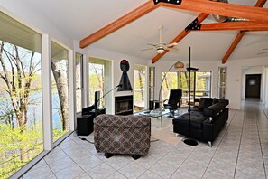 Ein geräumiges Wohnzimmer mit Kamin, großen Fenstern und einer hohen Decke mit freiliegenden Balken.